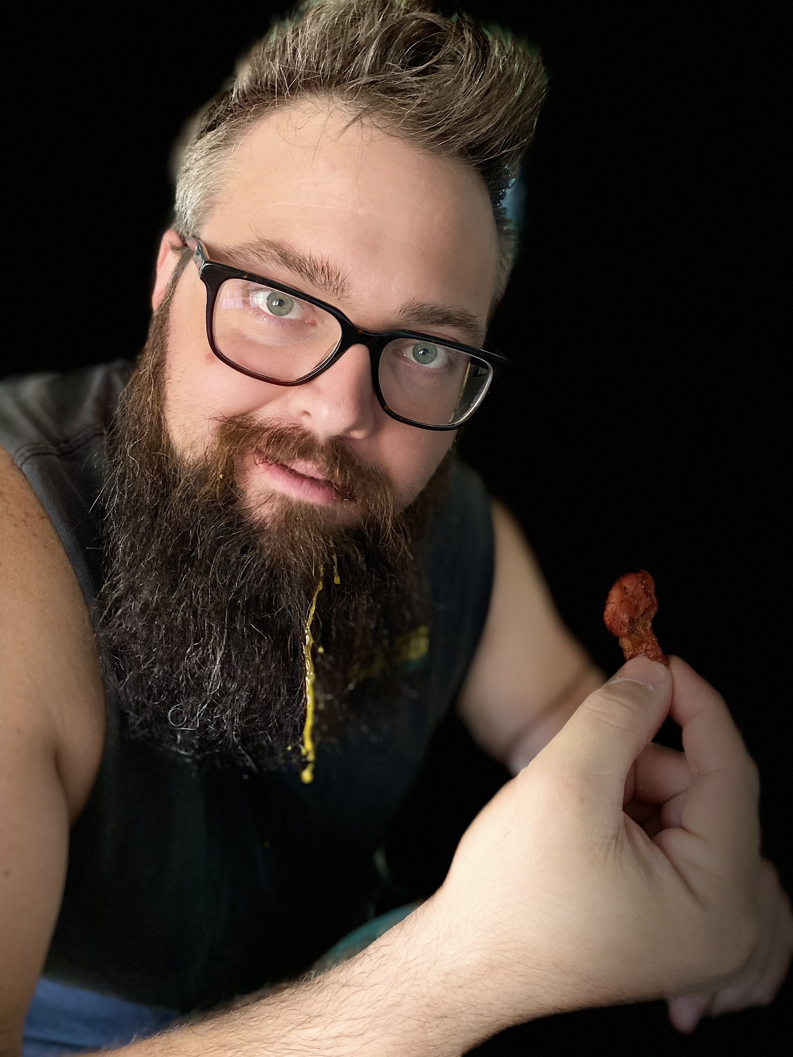 man holding a piece of bacon and posing to show the egg yolk running down his beard