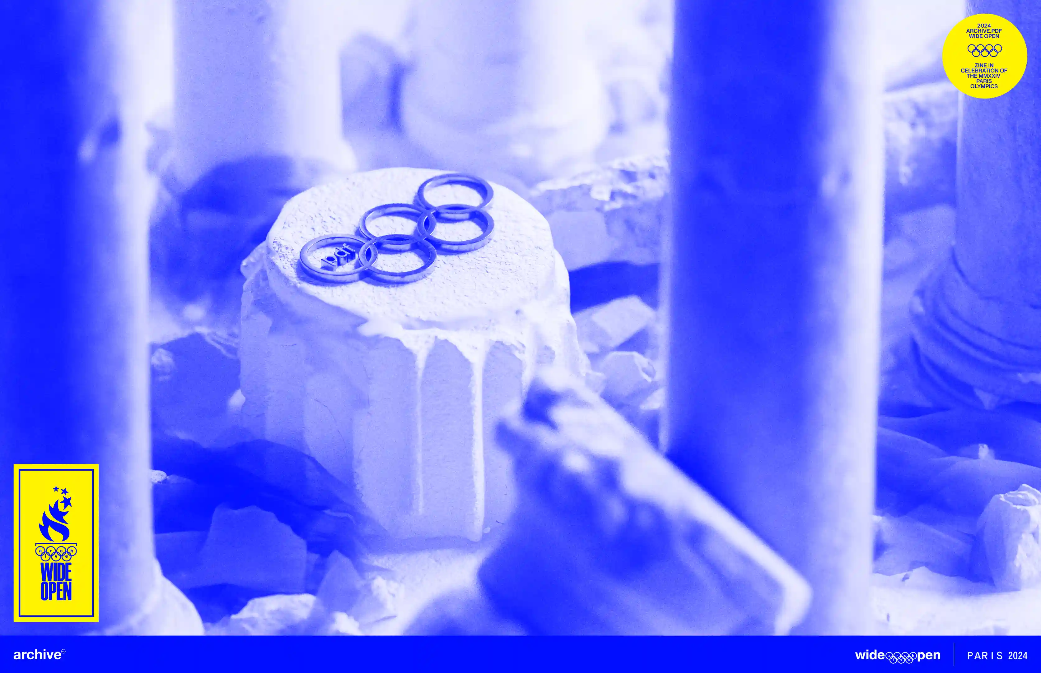 Archive PDF wide open Paris 2024 editorial cover image showing a white cake topped with Olympic style rings in a blue duotone colorway with the wide open Paris 2024 branding and yellow badge
