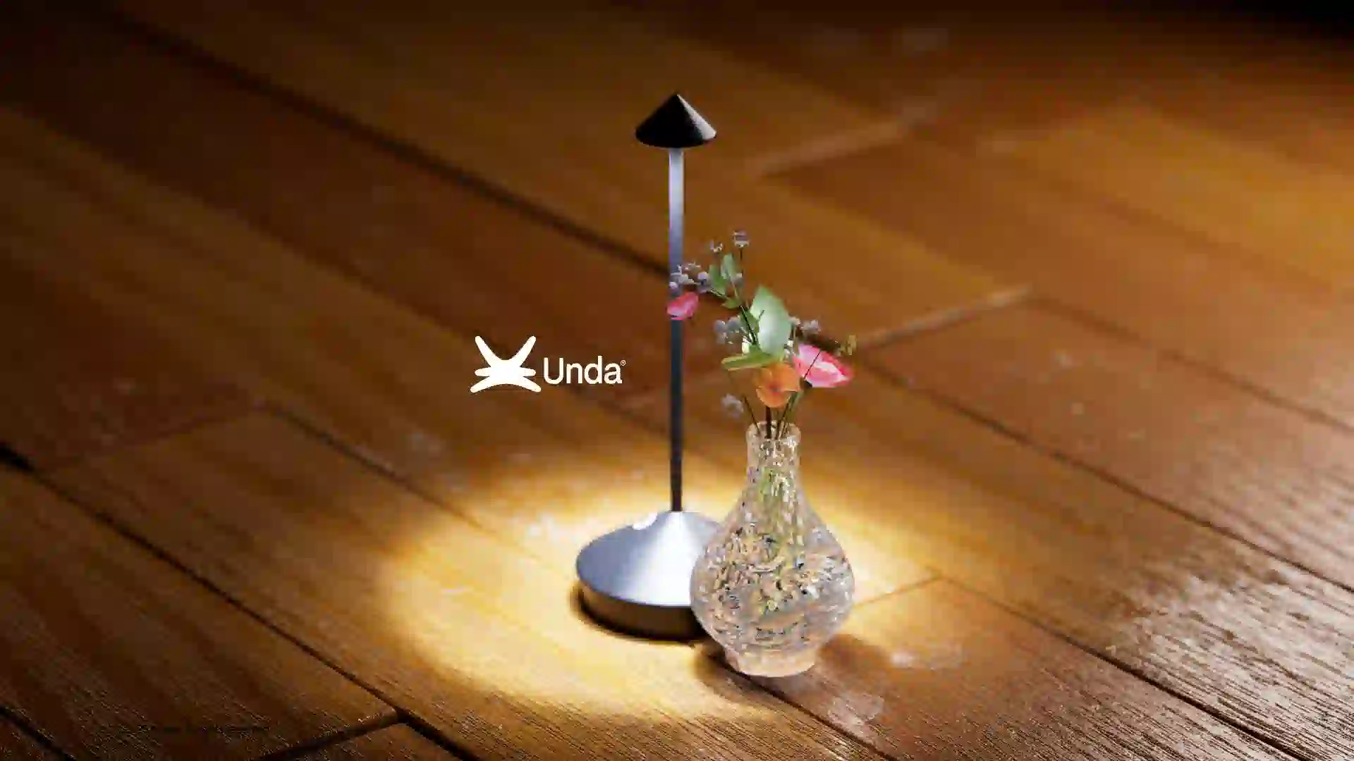 3D rendered minimalist black table lamp with warm glow next to a textured glass vase with flowers on a wooden floor Unda home goods concept