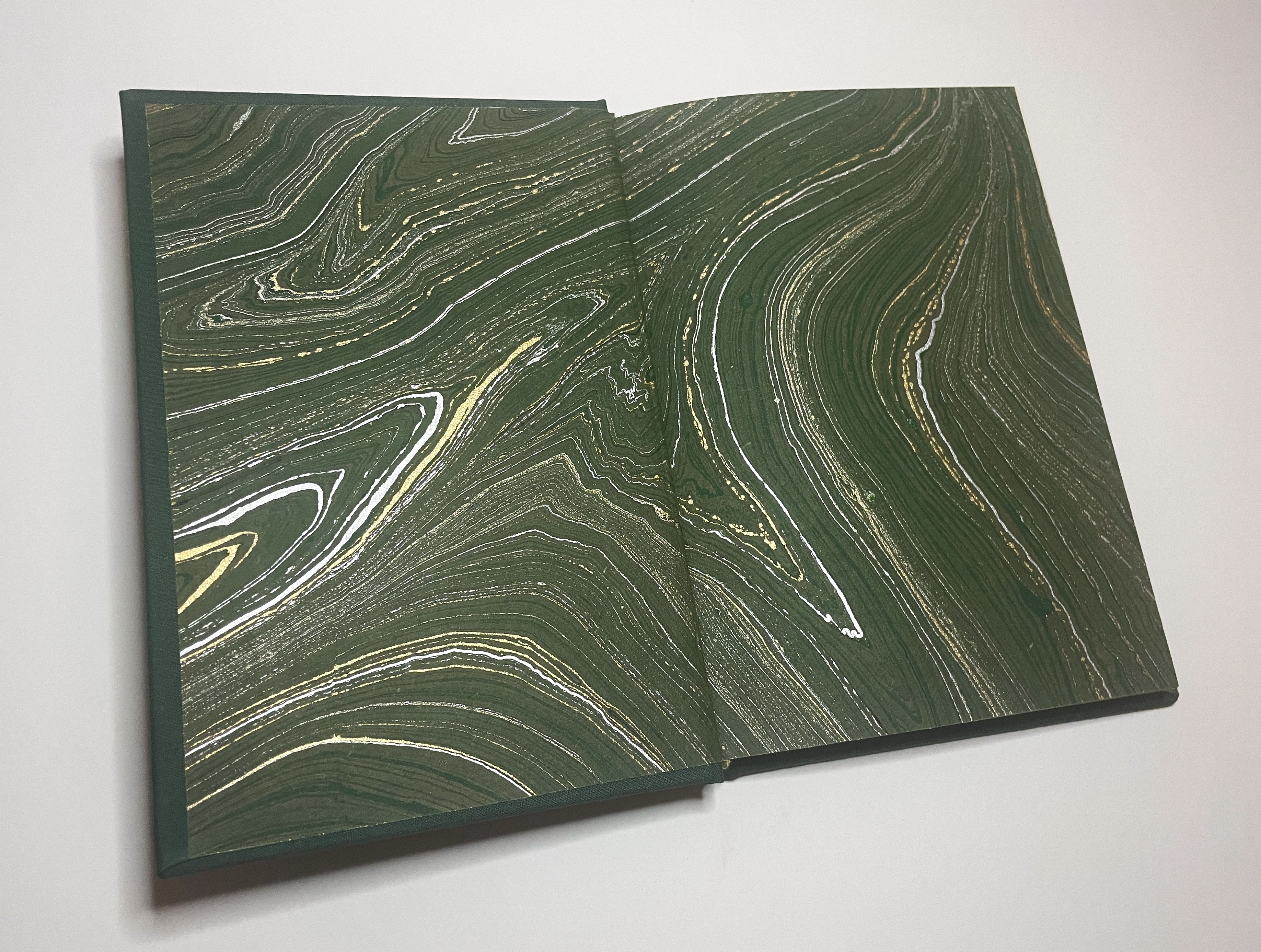 A hand-bound book open to the endpapers, which are green paper marbeled with white and gold paint.