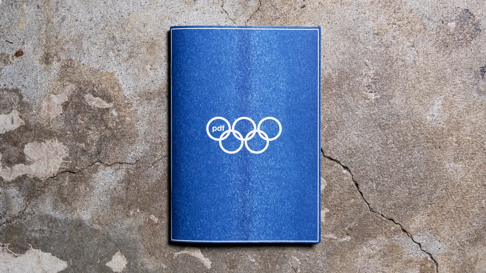 Archive PDF wide open Paris 2024 navy blue zine cover featuring the pdf Olympic five ring logo printed in white on a textured stone surface