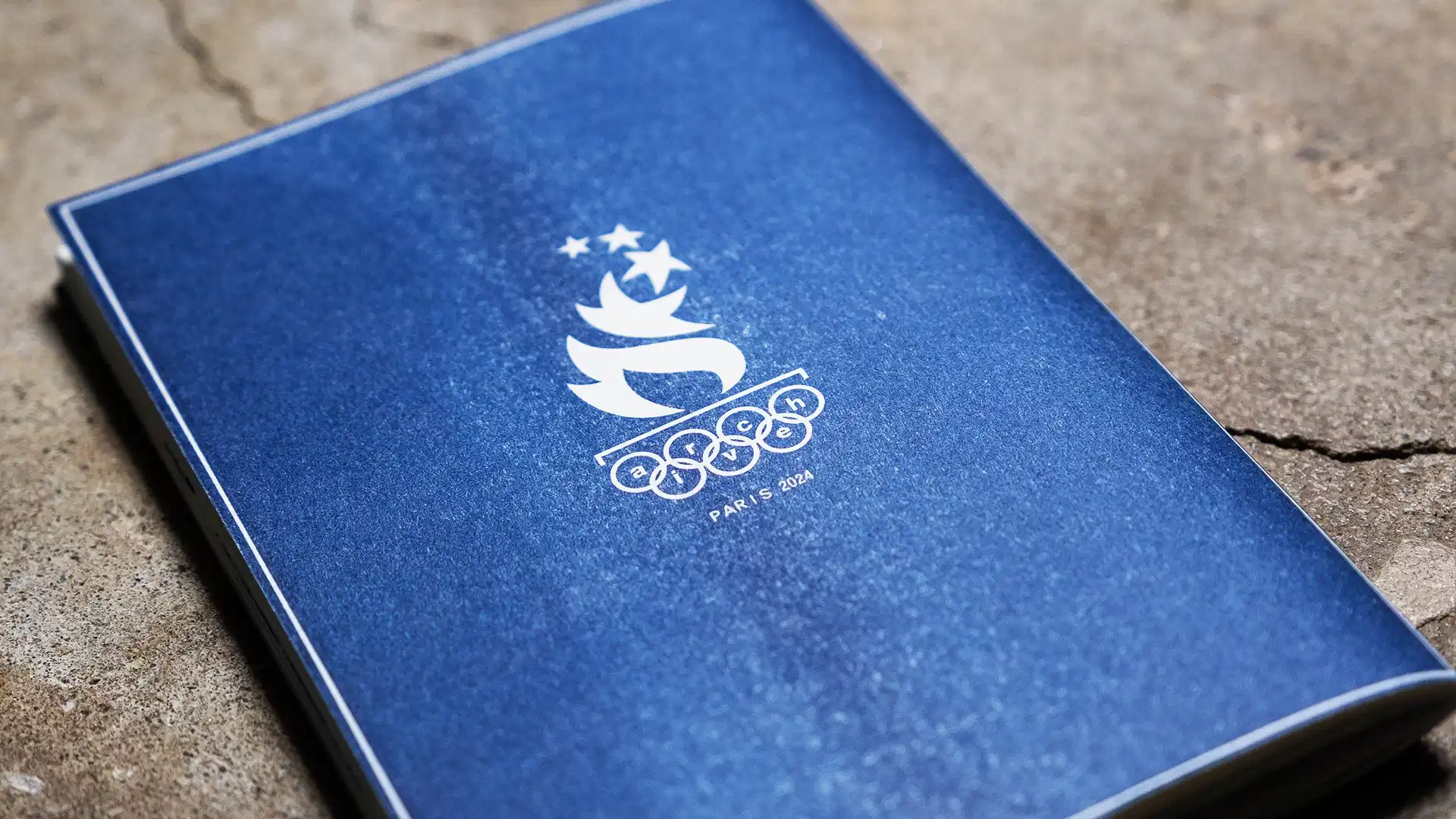 Archive PDF wide open Paris 2024 navy blue zine cover featuring the Paris Olympics flame and stars emblem with archive pdf lettering integrated into the rings on a stone surface
