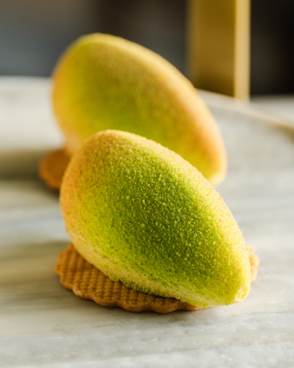 Bright and lush citrus mousse desserts with vibrant orange and green texture atop a delicate biscuit base, shot on a marble surface with soft flambient lighting.