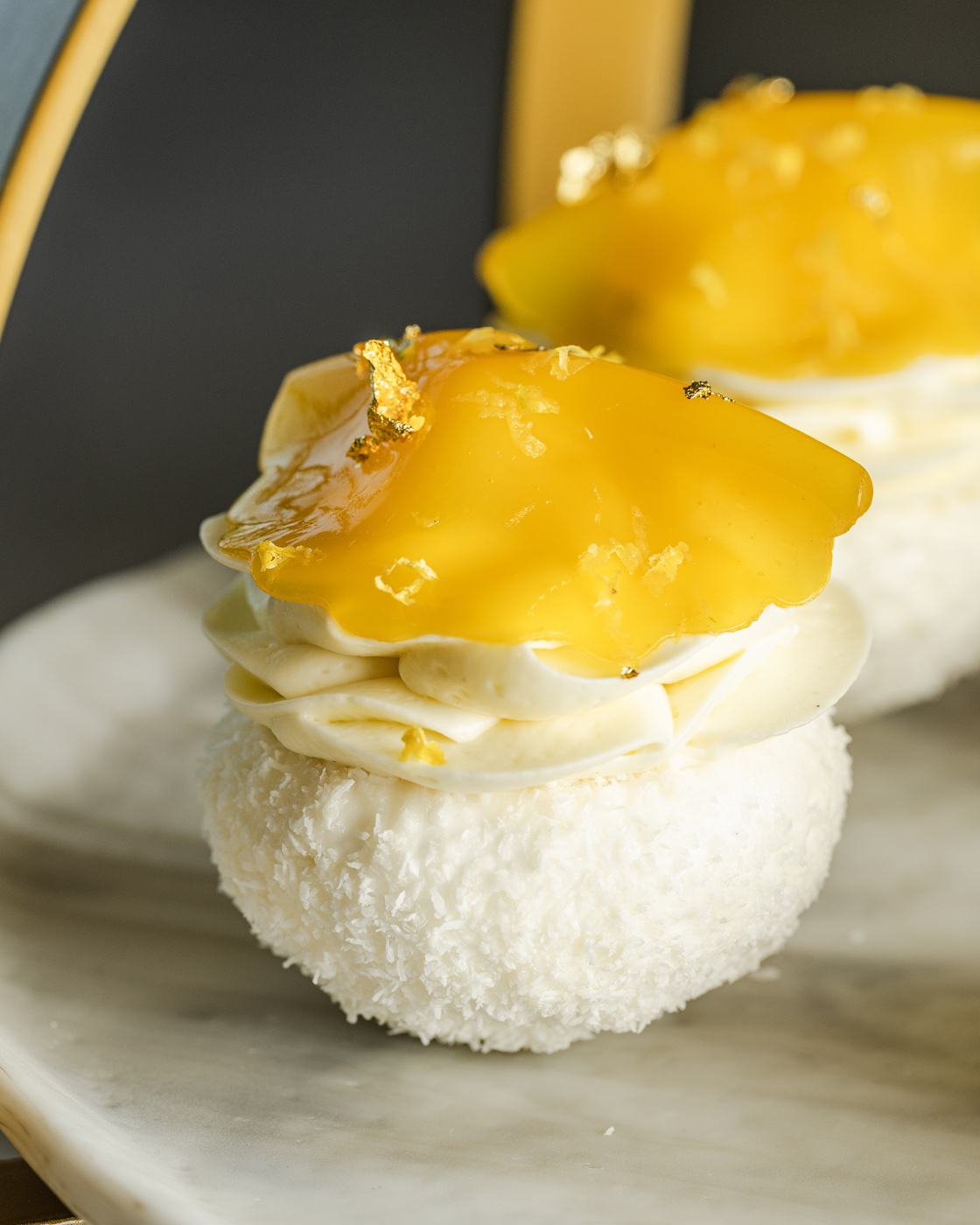 Close-up of an elegant dessert featuring a fluffy coconut base topped with rich mango puree and gold leaf embellishments, captured with soft lighting enhancing its creamy texture and luxurious appeal.