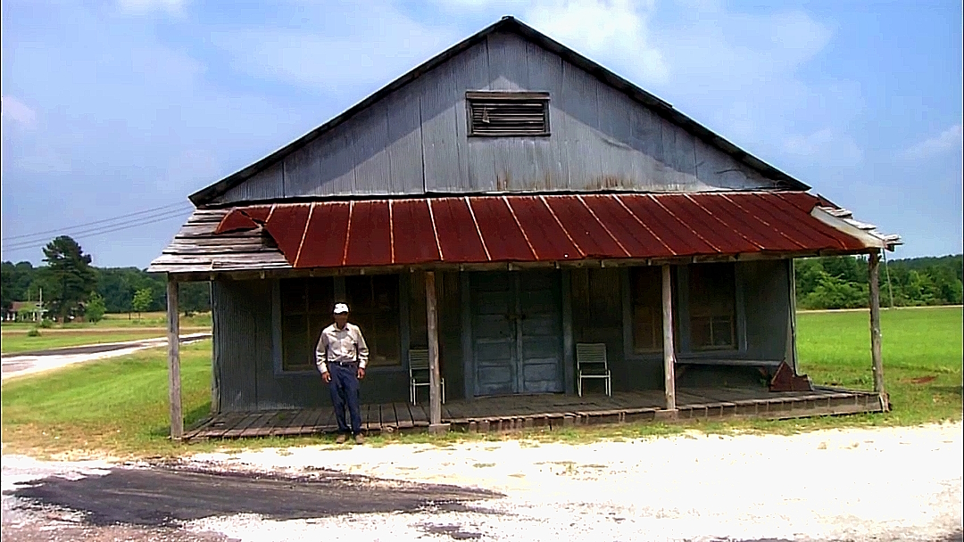 Figure 23: Thornton Dial standing in front of his childhood home in Emelle, Alabama. Video snapshot from Alabama Public Television.